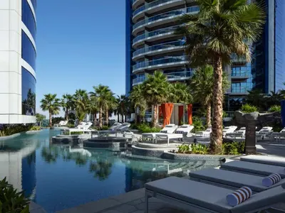 a resort pool with lounge chairs and palm trees at Cozy 2BR in Paramount Dubai with Burj Khalifa View in Dubai