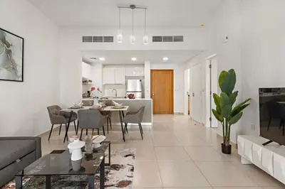 a white living room with a table and a kitchen at The Smart Concierge - Andalus Jumeirah Golf Estates in Dubai