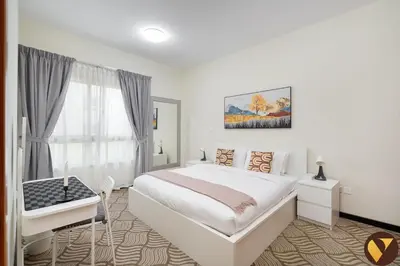 a white bedroom with a bed and a desk and a window at Vogue The Greens Al Alka near Mall of the Emirates, One Bedroom Apartment with Balcony and Vibrant community View, Access to all Amenities in Dubai