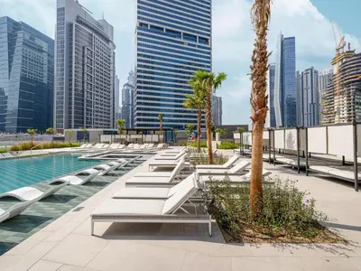 a pool with chaise lounges and a palm tree and buildings at Peninsula One Suites by Prestige Nest in Dubai