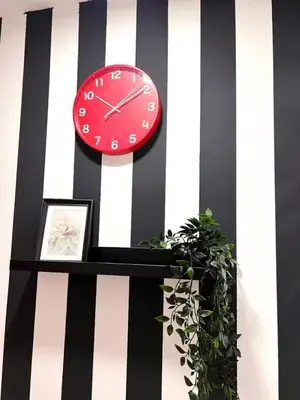 a red clock on a striped wall with a plant at Royal Budget Stay Dubai In Tecom Near Metro in Dubai