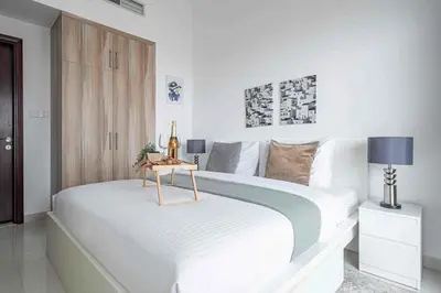 a white bedroom with a large bed with a table at Frank Porter - Hera Tower in Dubai