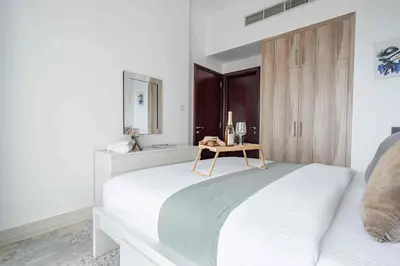 a white bedroom with a bed and a wooden cabinet at Frank Porter - Hera Tower in Dubai