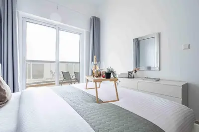 a white bedroom with a bed with a table and a window at Frank Porter - Hera Tower in Dubai