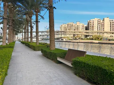 a park with a bench and palm trees and buildings at Serene Creek Harbour Escape with Burj Khalifa View in Dubai