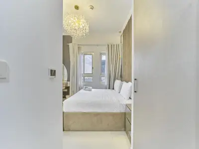 a bedroom with a white bed and a chandelier at Cozy 2BR Canal Residence Sports City in Dubai