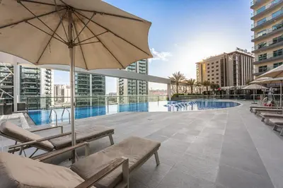 a patio with chairs and an umbrella and a pool at Stylish Bella Rose Stay Pool & Gym in Dubai