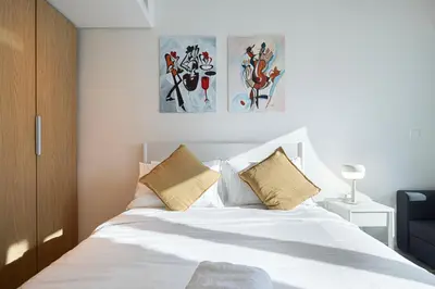 a bedroom with a white bed with three paintings on the wall at Luxury 1BR Lake View Near Metro & Marina in Dubai