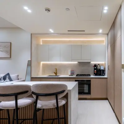 a kitchen with white cabinets and bar stools at Brand new apartment with luxury furniture in JVC in Dubai
