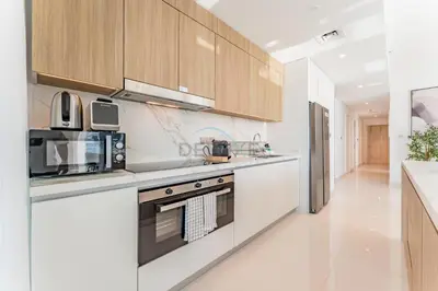 a kitchen with white appliances and wooden cabinets at Panoramic Sea View, Offering Direct Access to Beach, Three Bedrooms and Assistant Room - Beach Vista Tower 2 by Deluxe Holiday Homes in Dubai