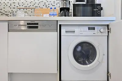 a white washing machine under a counter in a kitchen at Bloomfields Luxury 1BR, Damac Voleo, Business Bay in Dubai