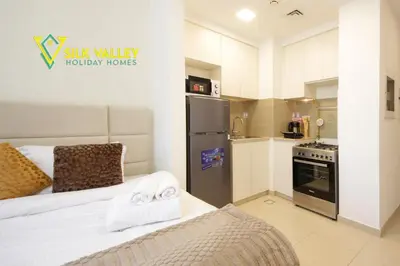 a small kitchen with a bed and a refrigerator at Silk Valley - Luxury Studio with Pool View - Walk to Park in Dubai