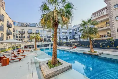 a swimming pool with palm trees and buildings at Urban Chic 1 Bedroom with big Balcony Kitchen in JVC in Dubai