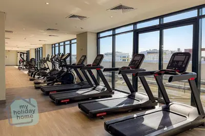 a row of treadmills in a gym with windows at Modern 1BR Azizi Riviera with Pool & Gym in Dubai