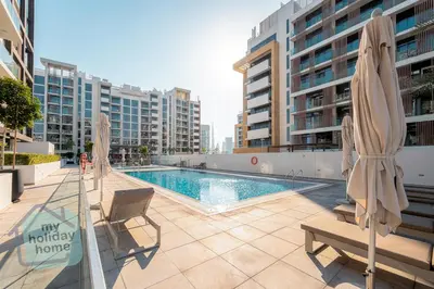 a swimming pool with chairs and umbrellas on a building at Modern 1BR Azizi Riviera with Pool & Gym in Dubai
