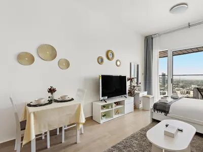 a white bedroom with a bed and a table and a tv at Spacious Studio w Sofa Bed Sleeps 4 in JVC in Dubai