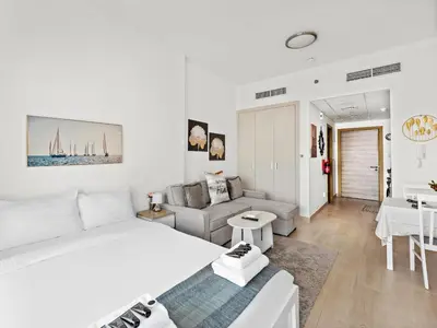 a white bedroom with a large bed and a living room at Spacious Studio w Sofa Bed Sleeps 4 in JVC in Dubai