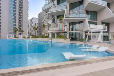 a swimming pool with two white chairs and a building at StayShort - Modern 1 Bedroom with Private Jacuzzi in JVC that Sleeps 2 in Dubai