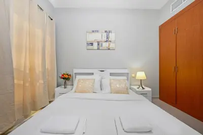 a white bedroom with a large white bed and a cabinet at Lake Point Tower 1 BHK by Petals Holiday Homes in Dubai
