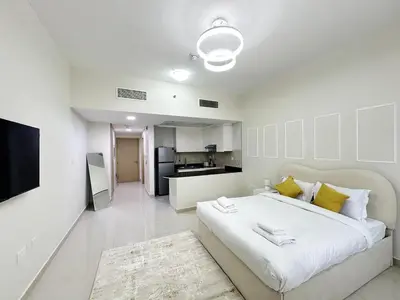 a white bedroom with a large bed and a kitchen at Profile Residency Studio near Dubai Stadium by Petals Holiday Homes in Dubai