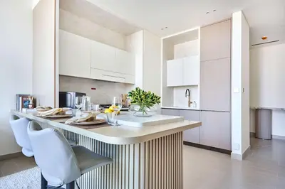 a kitchen with a counter with white cabinets and chairs at Frank Porter - Binghatti Phantom in Dubai