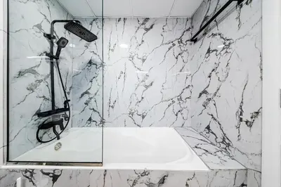 a bathroom with a shower with a white marble wall at New Bright Studio in Escan Tower, For 2, Dubai Marina in Dubai