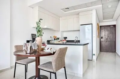 a white kitchen with a wooden table and chairs at Frank Porter - Damac Ghalia in Dubai
