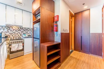 a kitchen with wooden cabinets and a refrigerator at Skyline Studio Overlooking the Community, Only a Few Steps from the Park, Al Jawhara Tower, Jumeirah Village Triangle by Deluxe Holiday Homes in Dubai