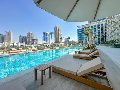a pool with chairs and a table next to a building at WelHome - Stylish Dubai Studio in Prime JVC Location in Dubai