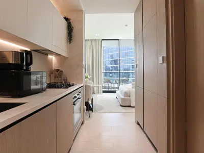a kitchen with white cabinets and a living room at WelHome - Stylish Dubai Studio in Prime JVC Location in Dubai