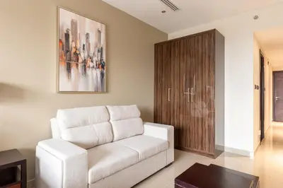 a living room with a white couch and a wooden cabinet at Elite Downtown Studio with Balcony & Pool in Dubai