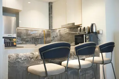 a kitchen with three bar stools in front of a counter at Well-Designed Modern 2 BHK Apartment Nobles Tower in Dubai