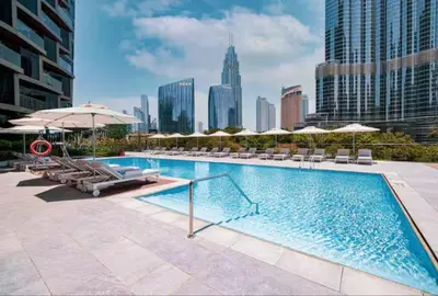 a swimming pool with chairs and umbrellas and a city at Vogue Downtown Address Residence near Burj Khalifa and Dubai Mall, Two Bedroom Apartment with Balcony and Burj Khalifa view, Access to all Amenities in Dubai