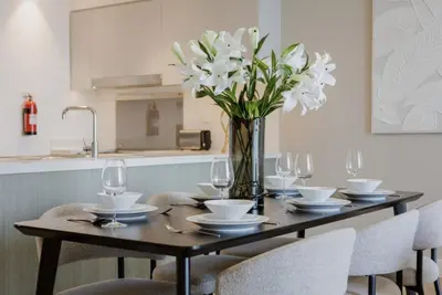 a table with chairs and a vase with white flowers at Grand Burj Vista Downtown Apartment with Burj Khalifa View in Dubai