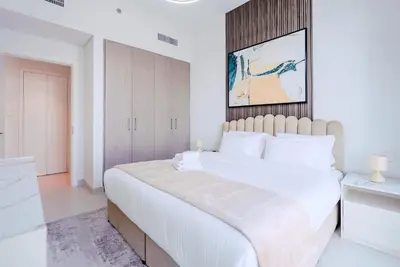 a white bedroom with a large bed and a cabinet at TRPS - The Grand, Dubai Creek Harbour - Luxury High-Floor 1BR, Creek & Skyline View in Dubai