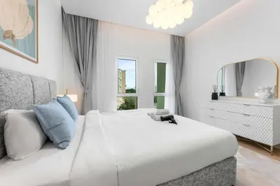 a white bedroom with a large bed and a mirror at StayShort - Chic Discovery Gardens 1Bed that Sleeps 2 in Dubai