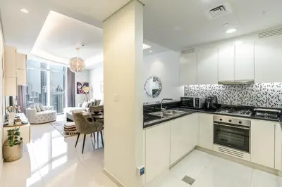 a kitchen with white cabinets and a living room at RH - Luxury 2BR at Paramount Midtown, Burj Khalifa View in Dubai