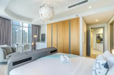 a bedroom with a large white bed and a living room at RH - Luxury 2BR at Paramount Midtown, Burj Khalifa View in Dubai