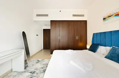 a bedroom with a white bed and a wooden cabinet at Modern 1BDR Apt With Balcony Pool Access And JVC in Dubai