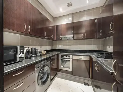 a kitchen with wooden cabinets and a washer and dryer at Livin' Holidays - 2 BR - Anantara Beach View in Dubai