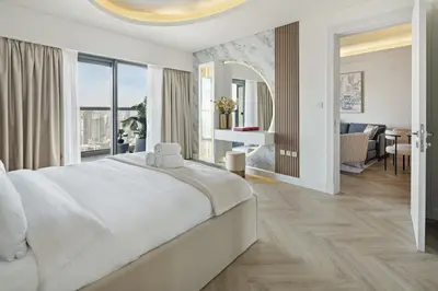 a white bedroom with a large bed and a living room at BurjKhalifaViews,1BHK, High Floor, Damac Paramount Tower B in Dubai