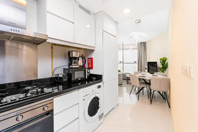 a kitchen with a washing machine and a dining room at Escape 24 Stylish 1BR in Artesia, Pool & Gym, Damac Hills in Dubai