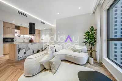 a living room with a white couch and a kitchen at Modern 1BR JBR Stunning Sea & Ain Dubai Views in Dubai