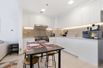 a kitchen with white cabinets and a table with stools at Safi Apartments 2A, Town Square - 2 Bedroom Apartment - Allsopp & Allsopp in Dubai