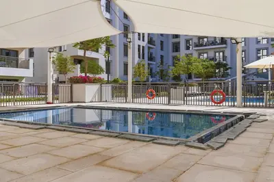 a swimming pool with an umbrella in front of a building at Safi Apartments 2A, Town Square - 2 Bedroom Apartment - Allsopp & Allsopp in Dubai