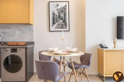 a kitchen with a table and chairs and a table and a dishwasher at Vogue JVT Novotel Near Springs Souk Mall, One Bedroom Apartment with Large Balcony and Vibrant Community view, Access to all Amenities in Dubai