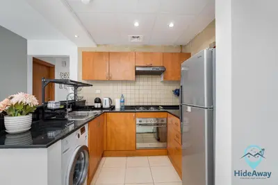 a kitchen with wooden cabinets and a stainless steel refrigerator at Elegant 1BR l Steps to Metro l Free Parking in Dubai