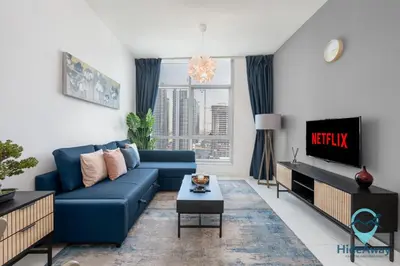 a living room with a blue couch and a tv at Elegant 1BR l Steps to Metro l Free Parking in Dubai