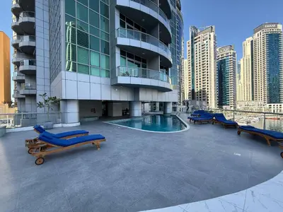 a large building with a swimming pool and blue lounge chairs at The Point Tower Dubai Marina in Dubai
