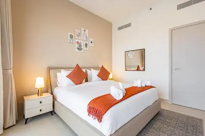 a bedroom with a large white bed with orange pillows at Superhost - 1BR Apartment , Pool & Gym , Near Dubai Hills Mall in Dubai
